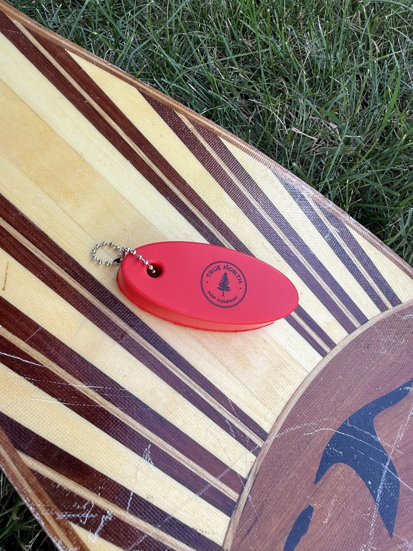 True North Map Co. floating keychain resting on a wooden canoe paddle